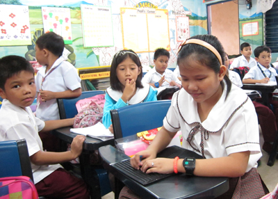 Girl using a slate in a classroom of curious children